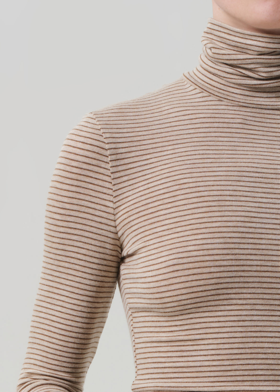 Person wearing a beige ribbed turtleneck sweater and brown leather pants on a light gray background