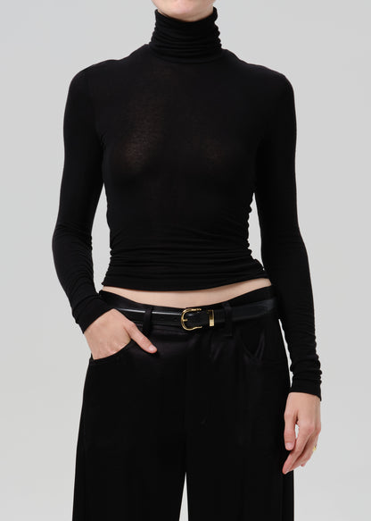 Person wearing a black fitted turtleneck with black wide leg trousers on a grey background