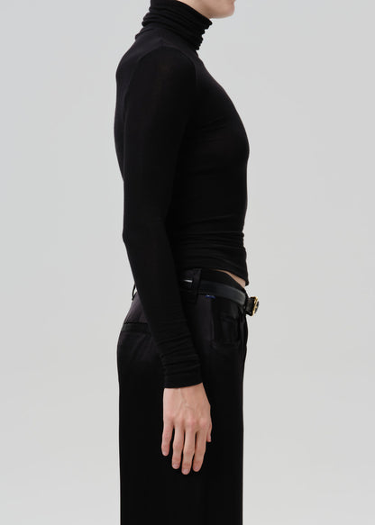 Person wearing a black fitted turtleneck with black wide leg trousers viewed from the side on a grey background