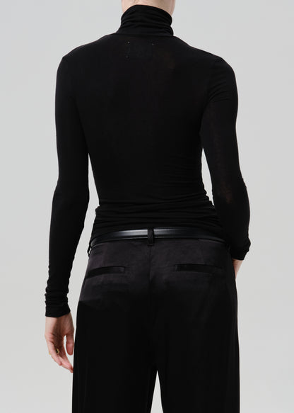 Person wearing a black fitted turtleneck with black wide leg trousers viewed from the back on a grey background