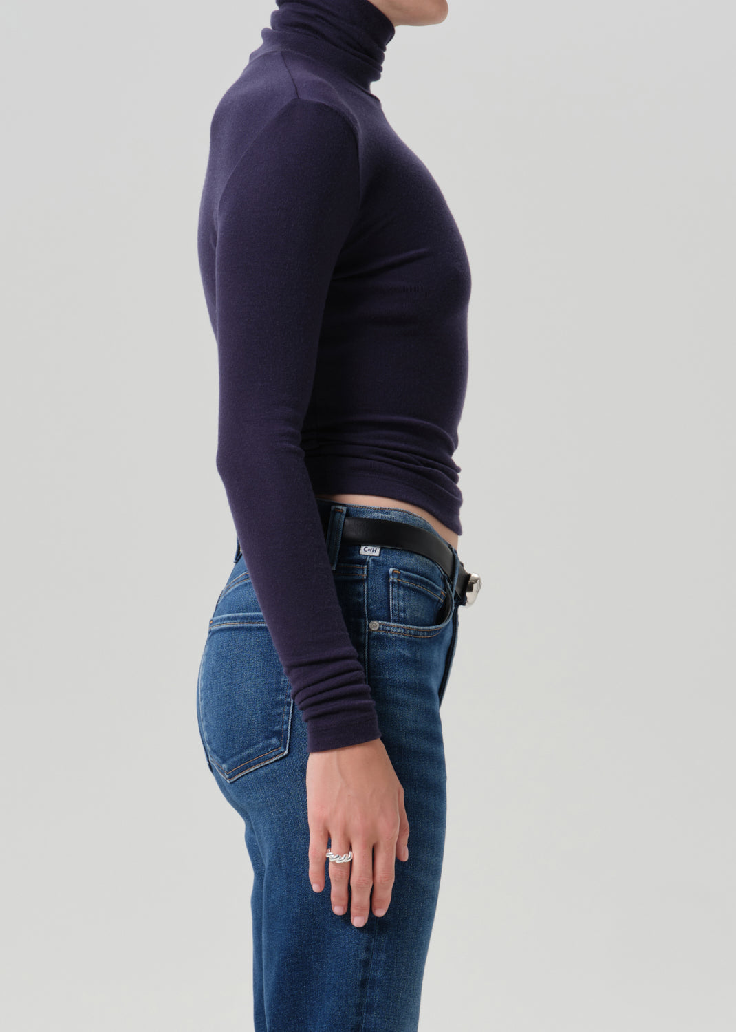 Person wearing a navy long sleeve turtleneck with dark wash straight leg jeans viewed from the side on a grey background
