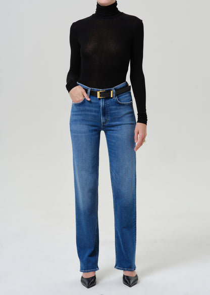 Woman wearing a black turtleneck top with medium blue straight leg jeans on a grey background.