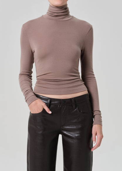 Person wearing a brown turtleneck and brown leather pants on a light gray background
