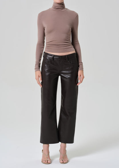 Person wearing a brown turtleneck and brown leather pants on a light gray background