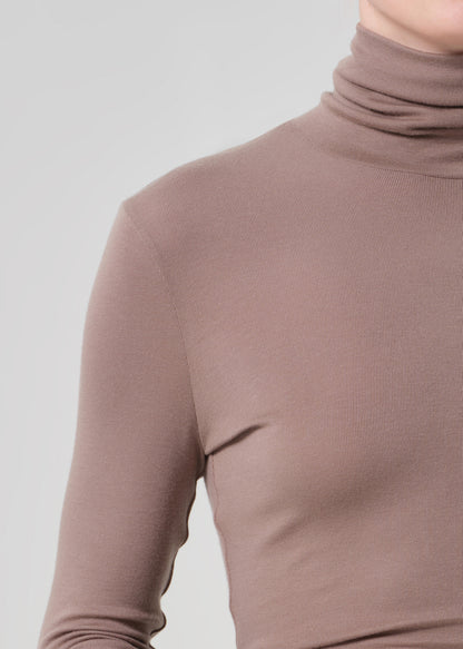 Person wearing a brown turtleneck and brown leather pants on a light gray background
