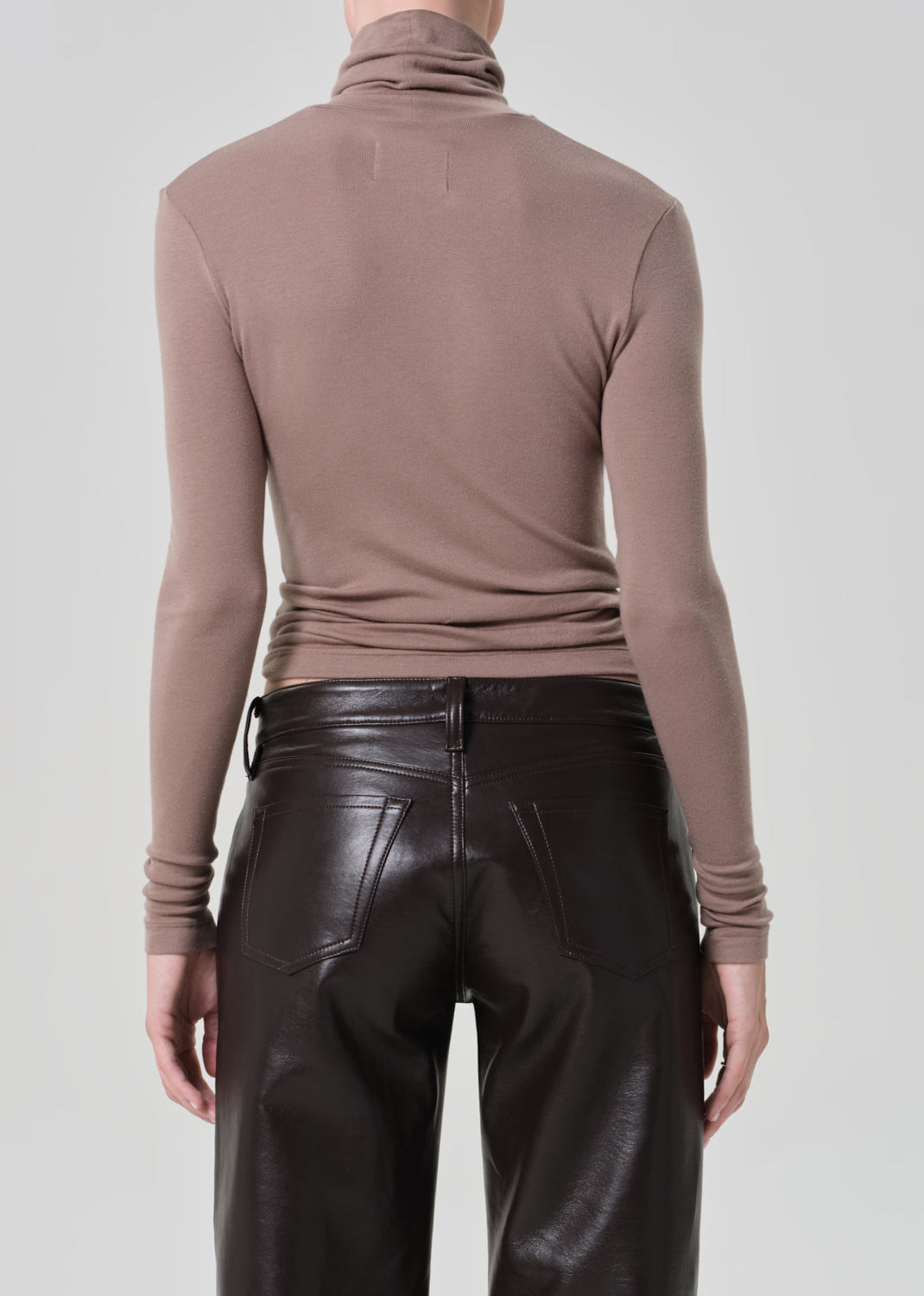 Person wearing a brown turtleneck and brown leather pants on a light gray background