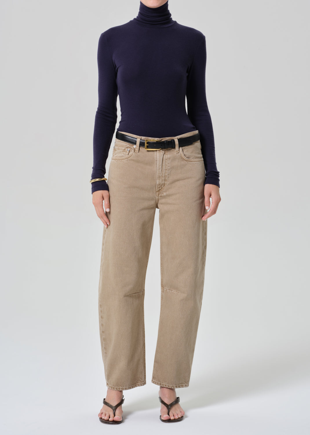 Person wearing a navy turtleneck and beige pants on a grey background