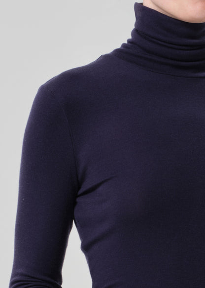 Person wearing a navy turtleneck and beige pants on a grey background