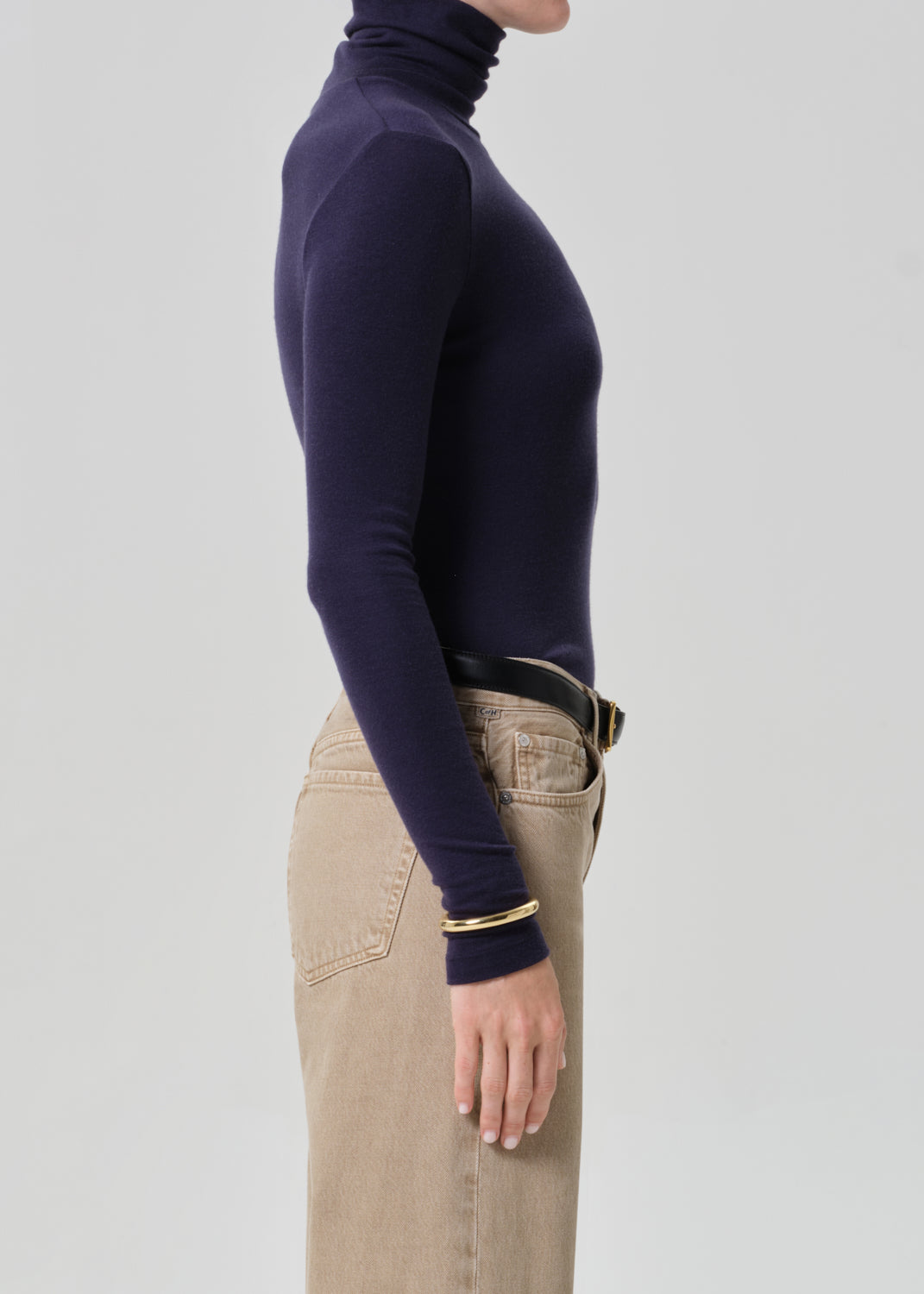 Person wearing a navy turtleneck and beige pants on a grey background