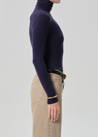 Person wearing a navy turtleneck and beige pants on a grey background