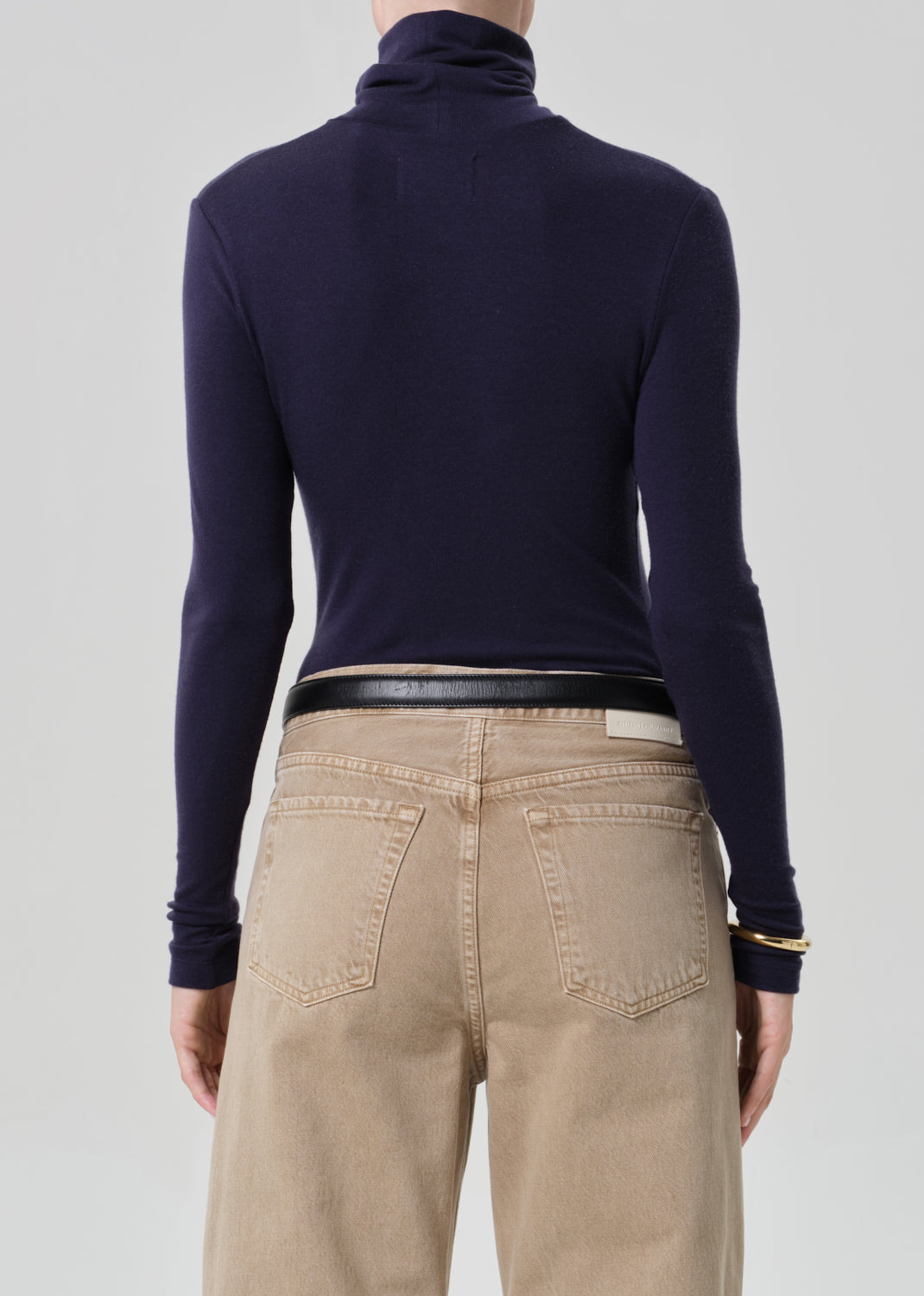 Person wearing a navy turtleneck and beige pants on a grey background