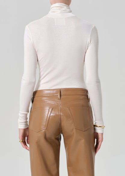 Person wearing a white turtleneck and brown leather pants on a gray background