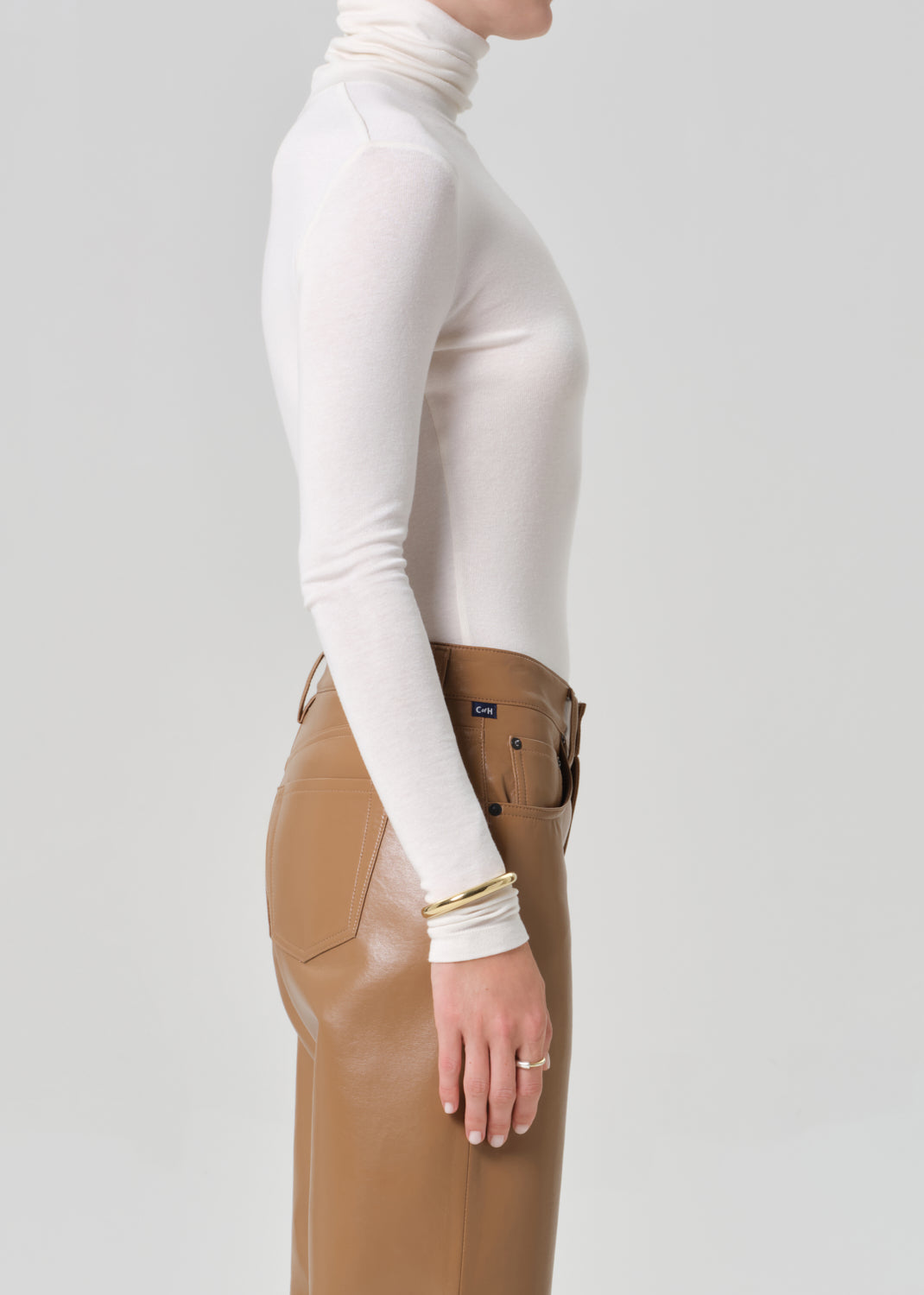 Person wearing a white turtleneck and brown leather pants on a gray background