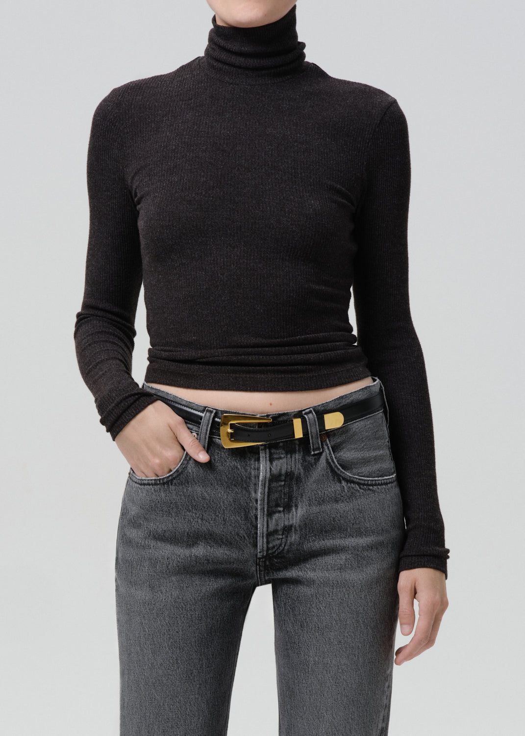 Person wearing a black ribbed long sleeve turtleneck on a grey background