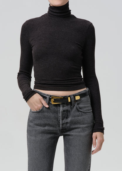 Person wearing a black ribbed long sleeve turtleneck on a grey background