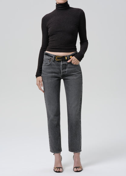 Person wearing a black ribbed long sleeve turtleneck with grey straight leg jeans on a grey background