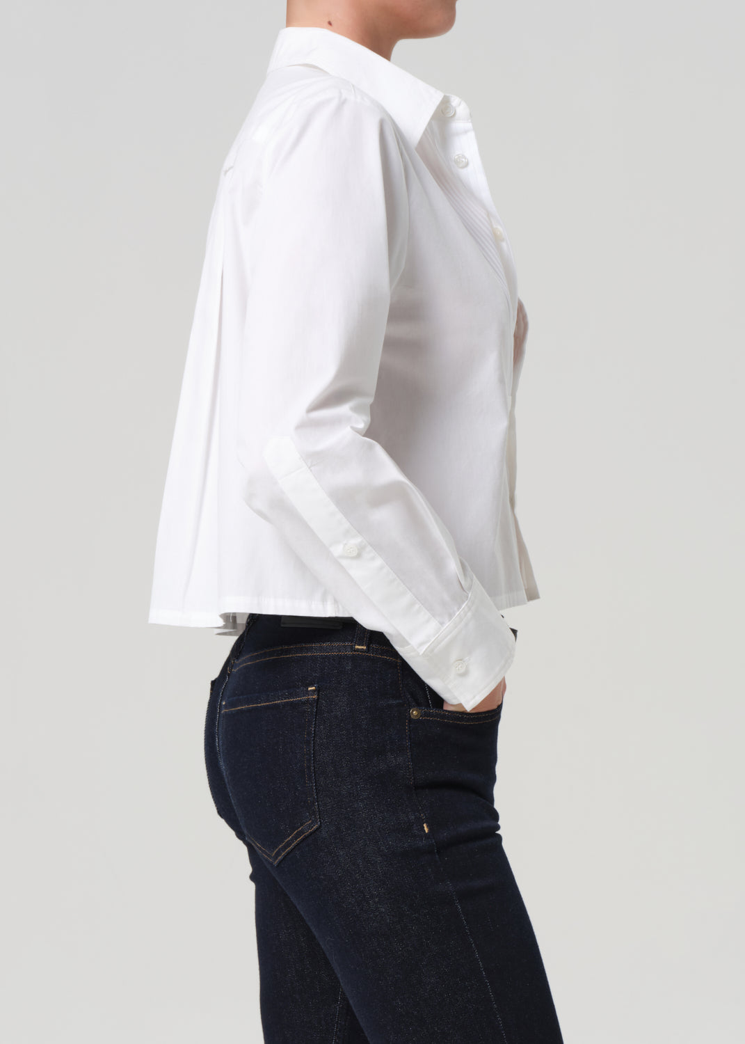 Person wearing a white shirt and dark jeans on a light gray background