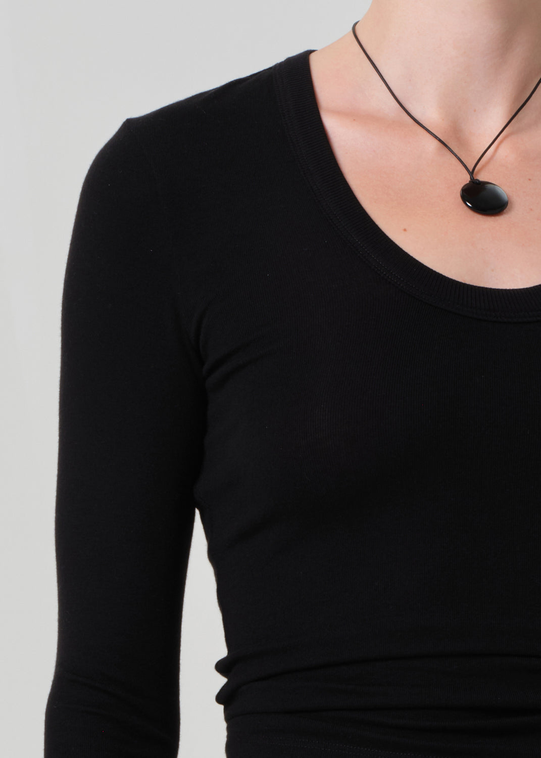 Person wearing a black long-sleeve top with a necklace on a plain background