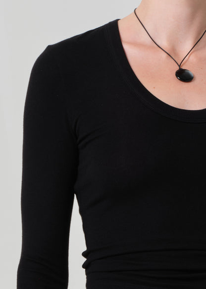 Person wearing a black long-sleeve top with a necklace on a plain background