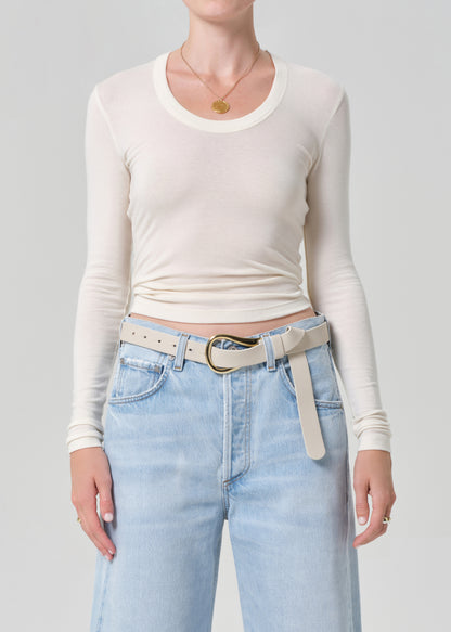 Person wearing a white long-sleeve top and light blue jeans with a belt on a gray background