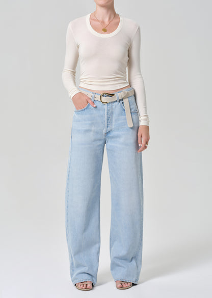 Person wearing light blue jeans and a cream long-sleeve top on a grey background