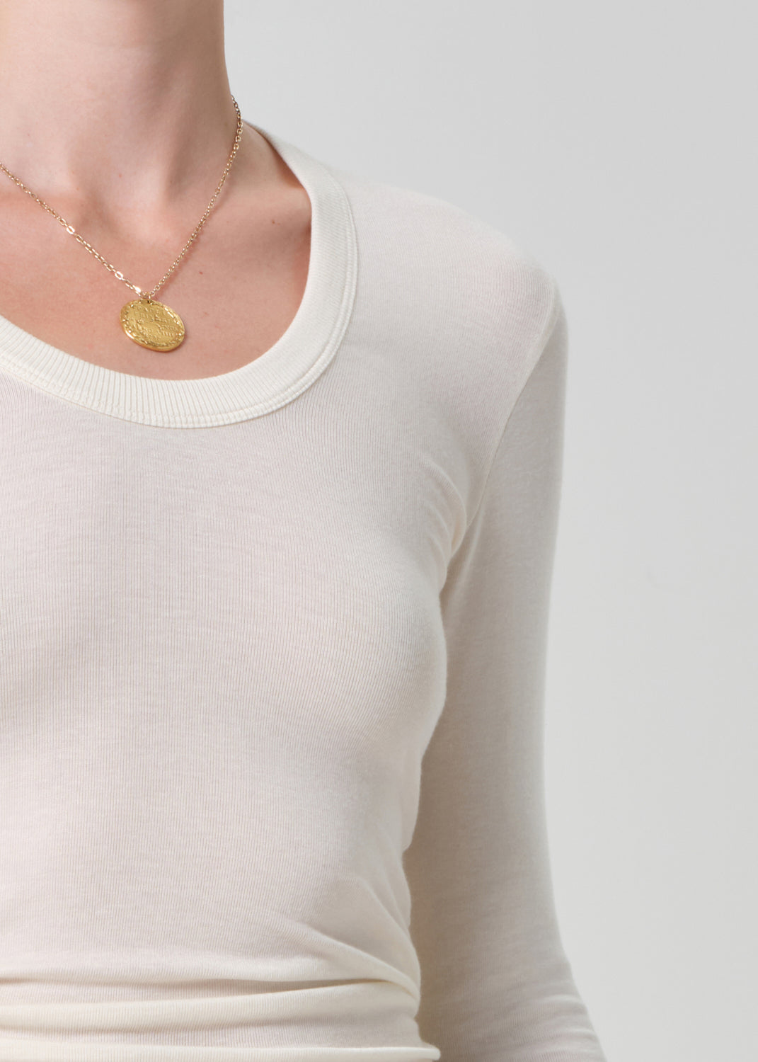 Person wearing a gold necklace with a coin pendant on a plain background