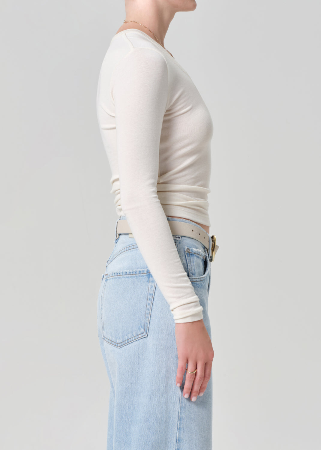 Person wearing a white long-sleeve top and light blue jeans on a plain background