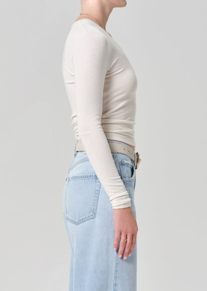 Person wearing a white long-sleeve top and light blue jeans on a plain background