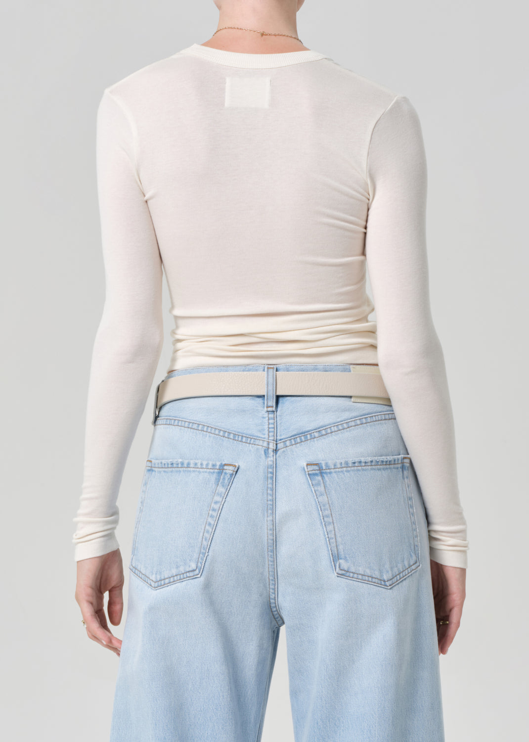 Person wearing a cream long-sleeve top and light blue jeans on a gray background