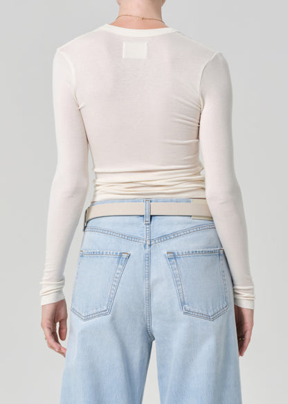 Person wearing a cream long-sleeve top and light blue jeans on a gray background