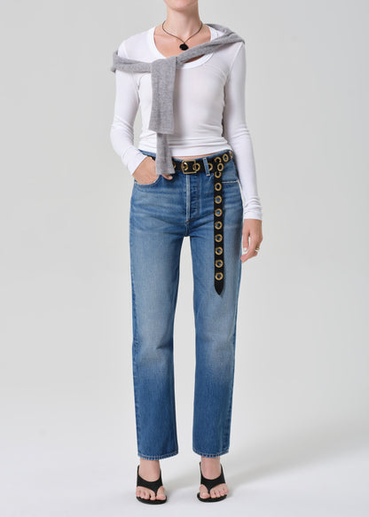 Person wearing a white long-sleeve shirt, gray sweater, and blue jeans with a decorative belt on a light gray background.