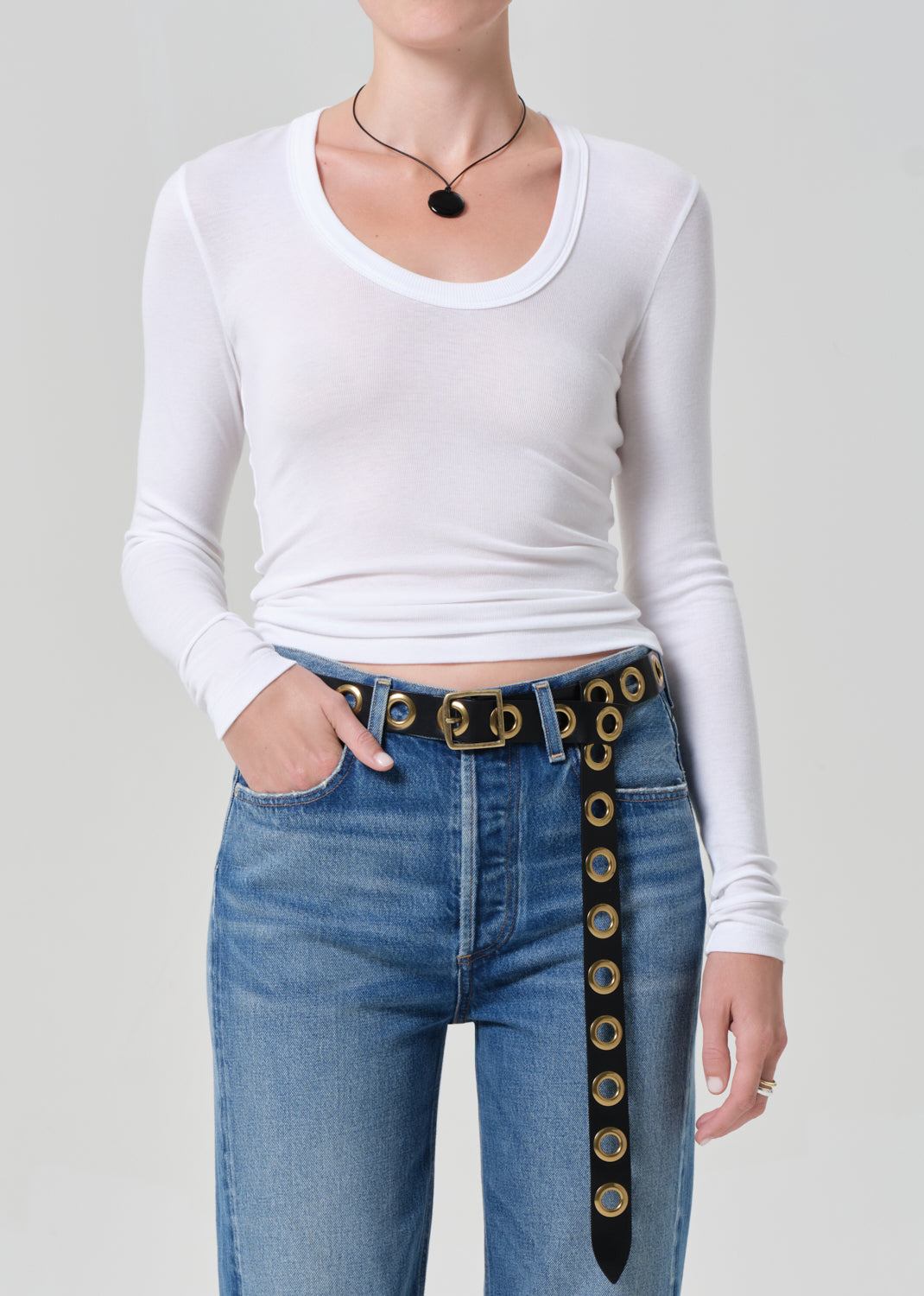 Person wearing a white long-sleeve top and blue jeans with a decorative belt on a plain background