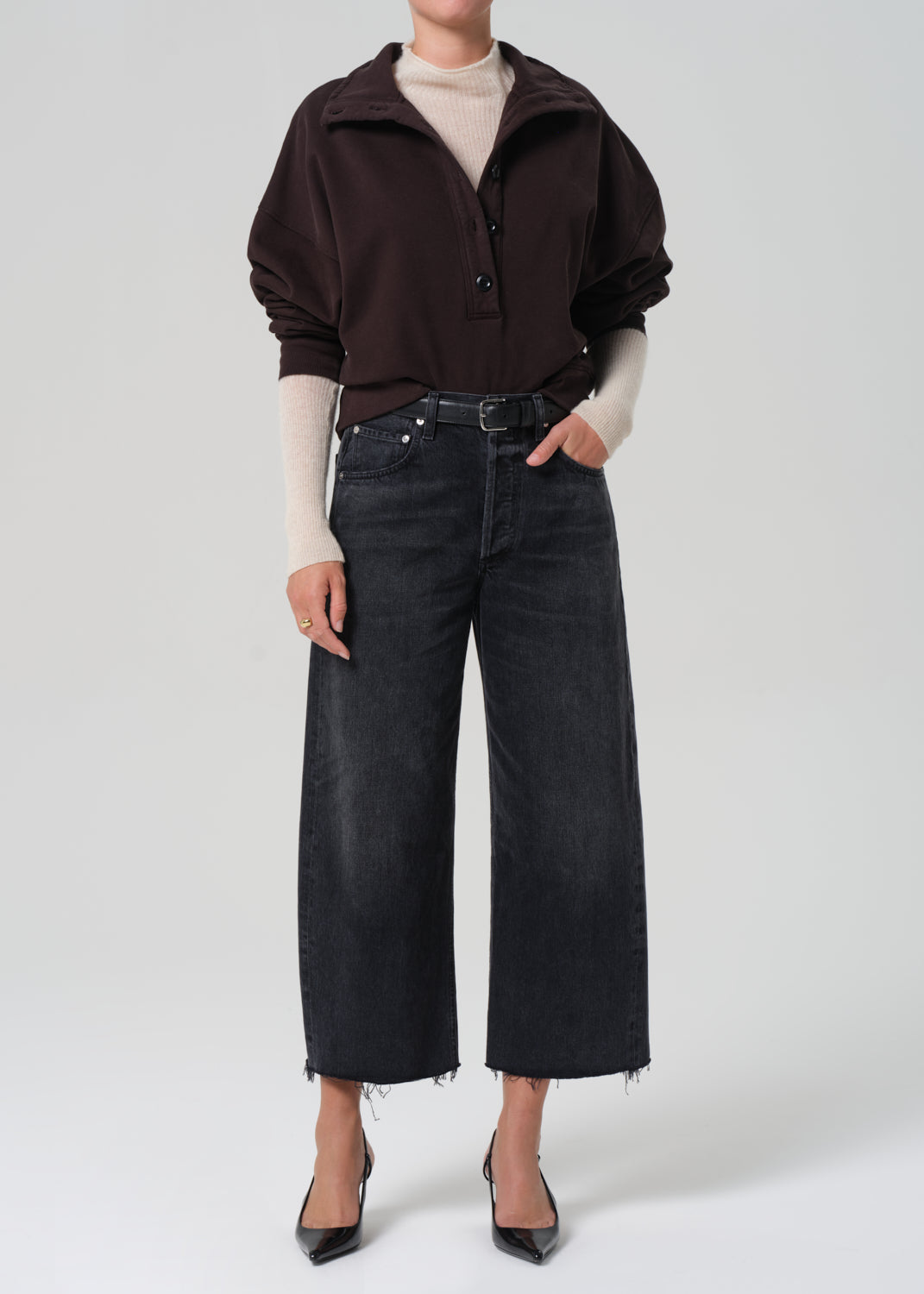 Person wearing a dark brown sweatshirt , white sweater, and black jeans on a white background