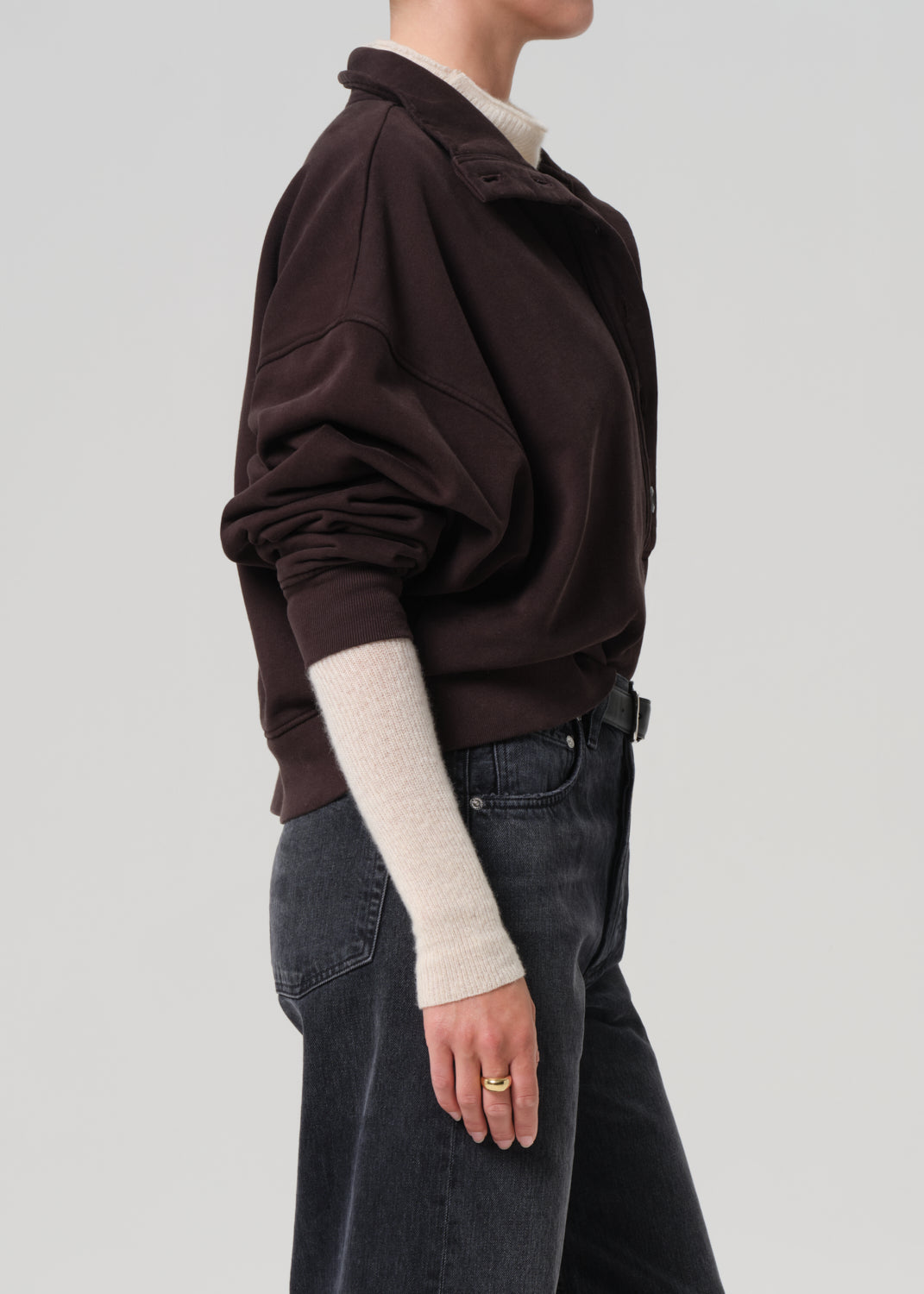 Person wearing a brown sweatshirt and dark jeans on a plain background
