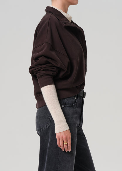 Person wearing a brown sweatshirt and dark jeans on a plain background