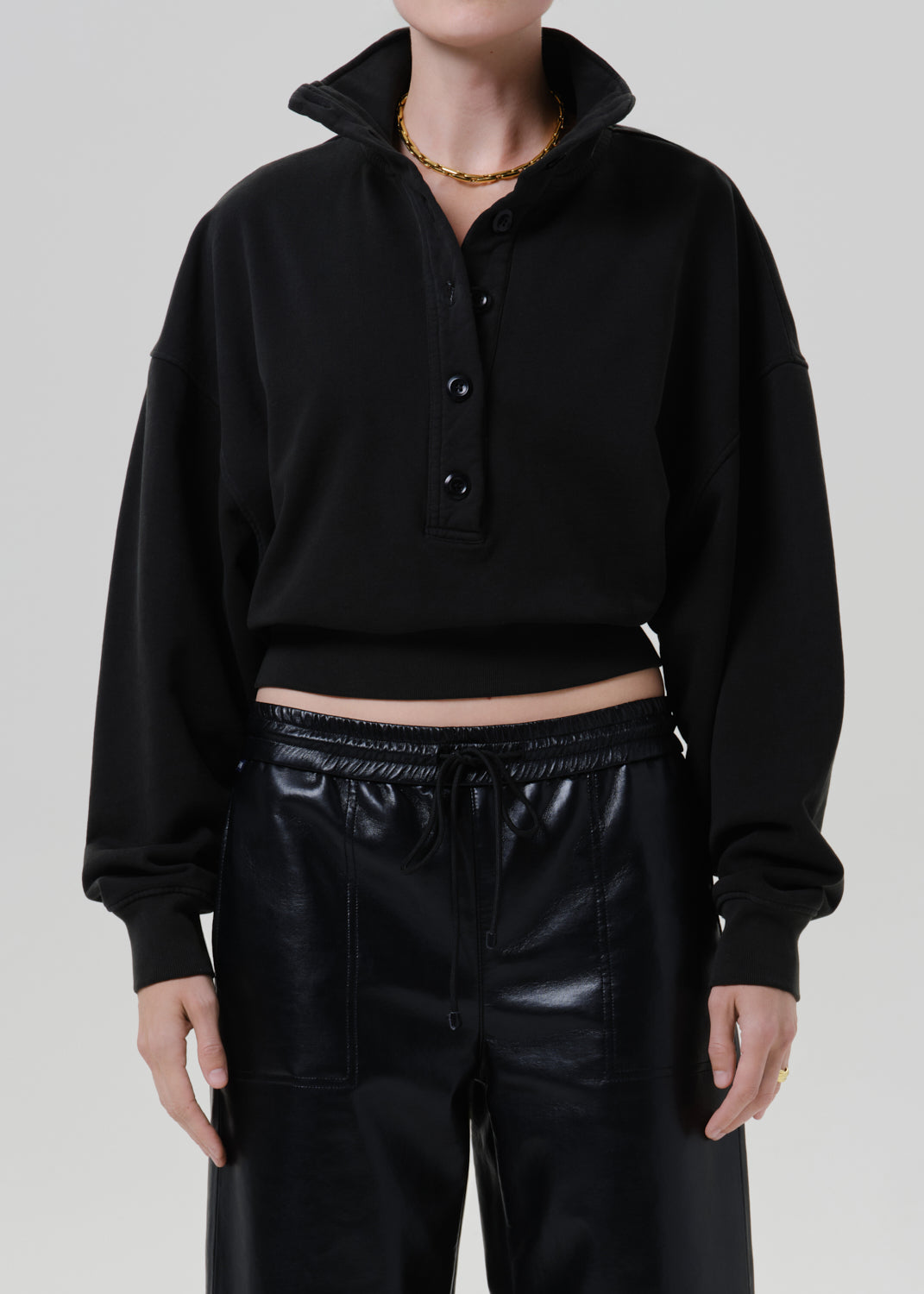 Person wearing a black long sleeve collared pullover with black leather pants on a grey background