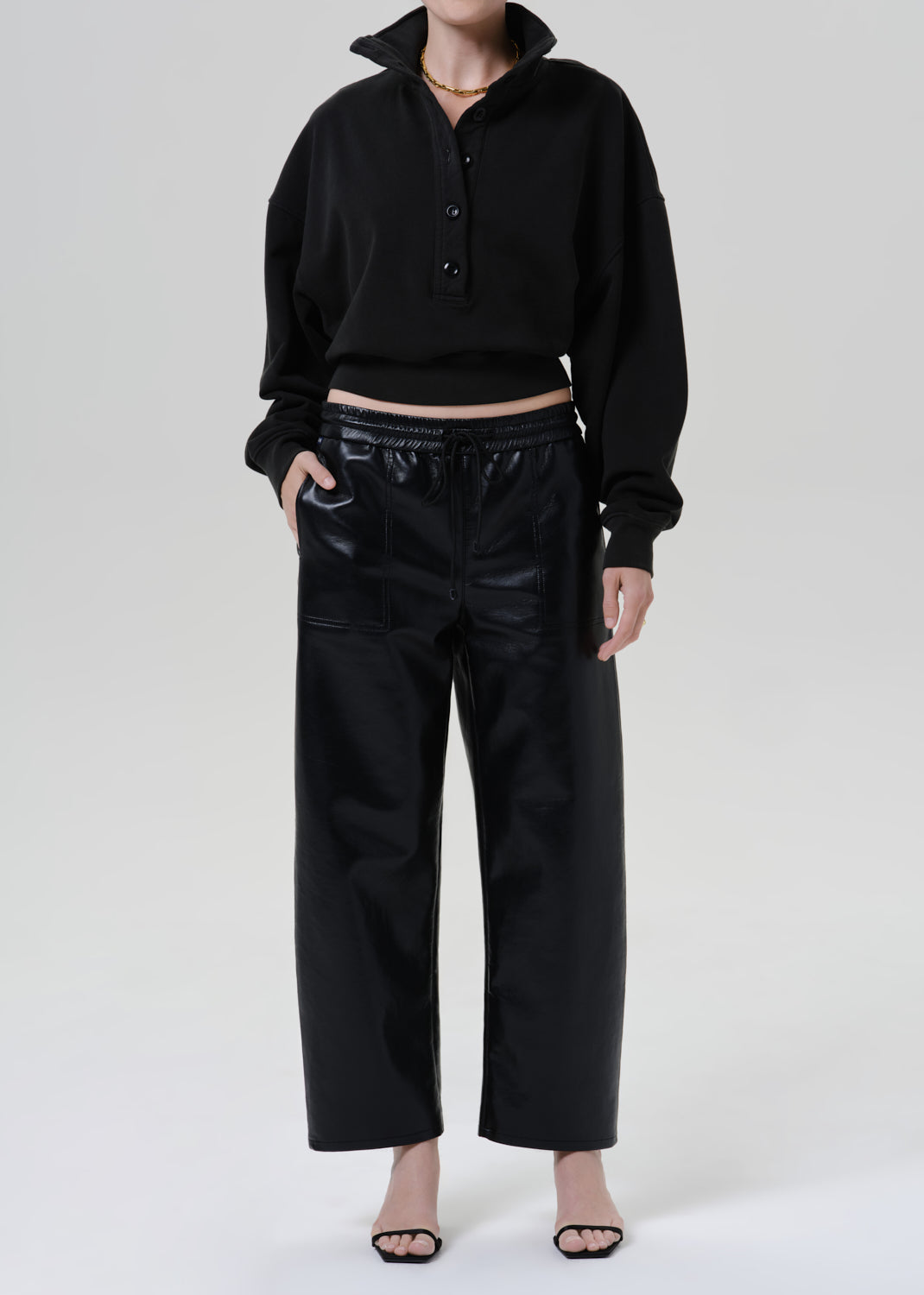 Person wearing a black long sleeve collared pullover with black leather pants on a grey background