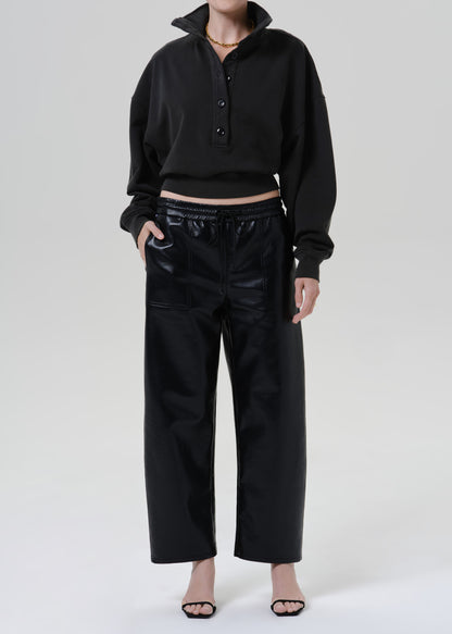 Person wearing a black long sleeve collared pullover with black leather pants and black heels, front full body view on a grey background.