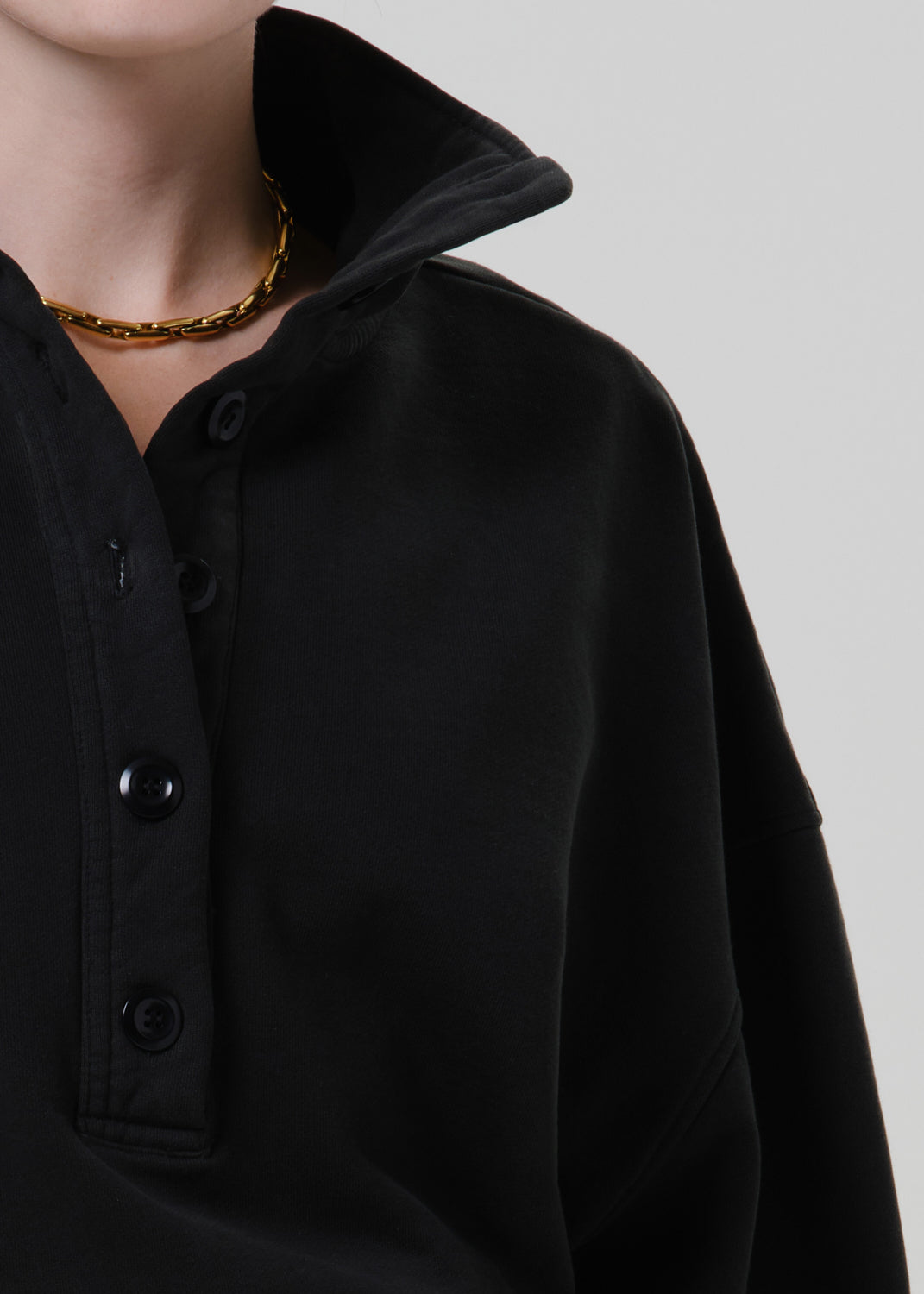 Person wearing a black long sleeve collared pullover on a grey background