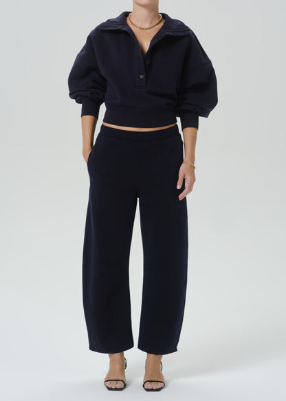 A model wearing a dark navy blue two-piece lounge set consisting of a cropped long-sleeve henley top with puffed sleeves and matching wide-leg cropped pants, styled with neutral sandals and gold jewelry against a grey background.