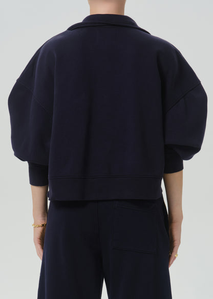 Back view of a person wearing a dark navy cropped sweatshirt with voluminous balloon sleeves and matching dark pants, against a grey background.