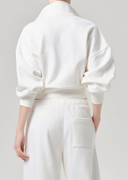 A model shown from the back wearing a white high-neck sweatshirt and matching white sweatpants against a grey background.