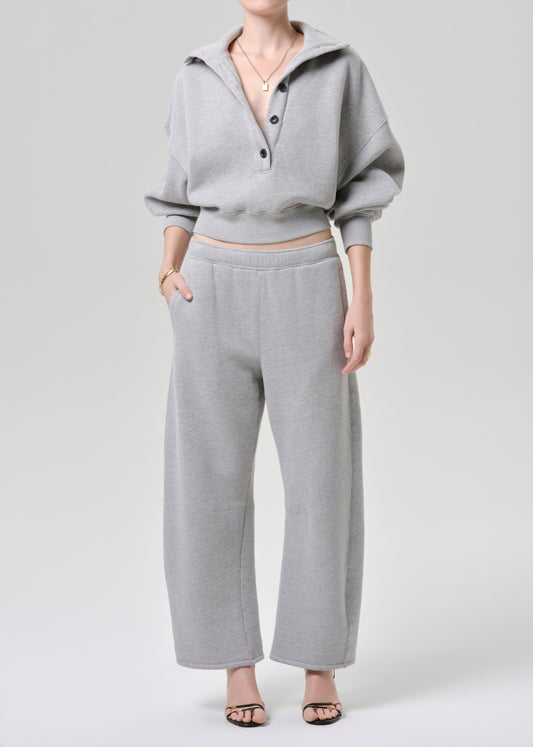 A model wearing a light grey two-piece loungewear set consisting of a cropped long-sleeve henley top and matching wide-leg sweatpants, photographed against a grey background.