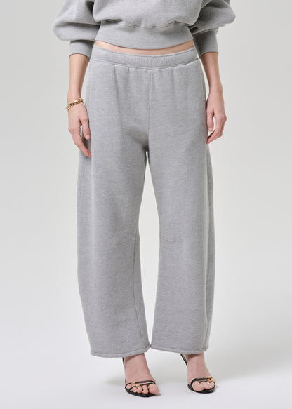 A model wearing light grey wide-leg sweatpants and a matching gray cropped sweatshirt, paired with black strappy heels, against a light grey studio background.