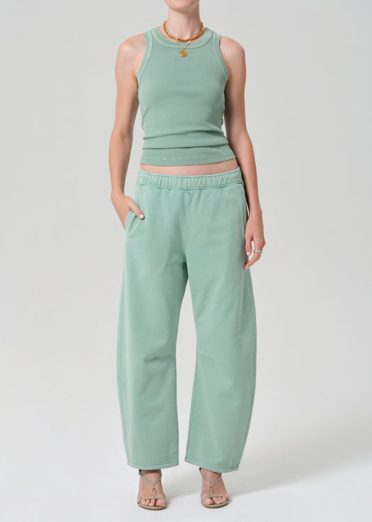 Person wearing a mint green sleeveless tank and matching green sweatpants on a grey background