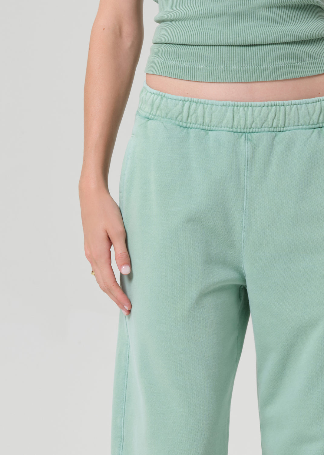 Person wearing a mint green sleeveless tank and matching green sweatpants on a grey background