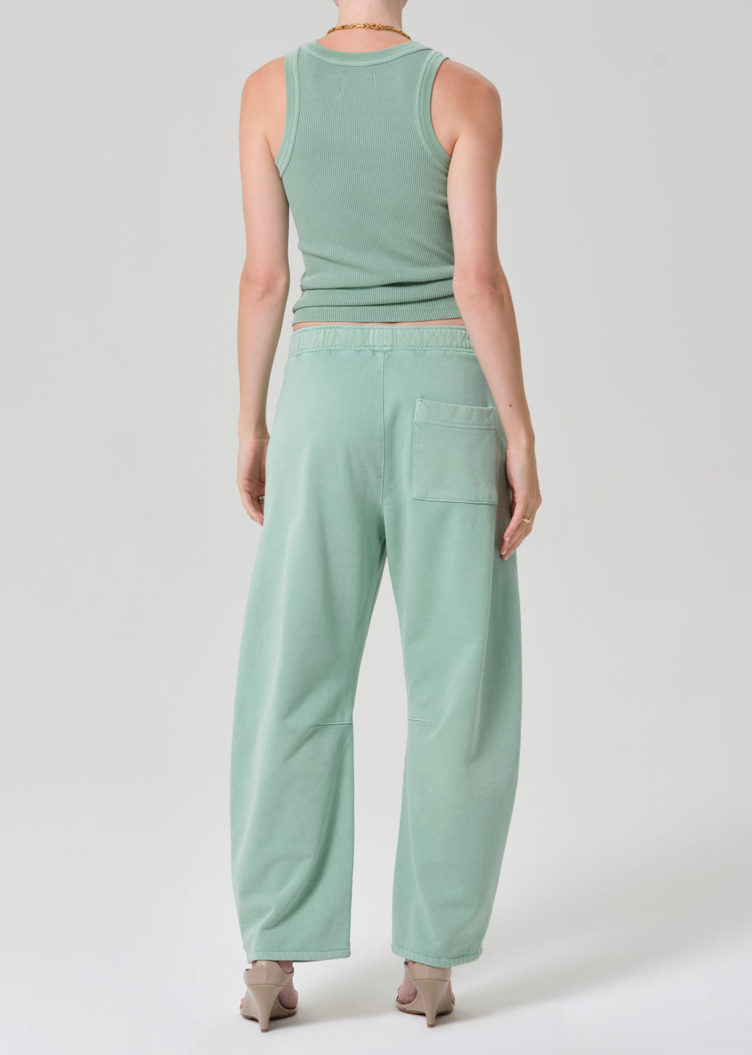Person wearing a mint green sleeveless tank and matching green sweatpants on a grey background
