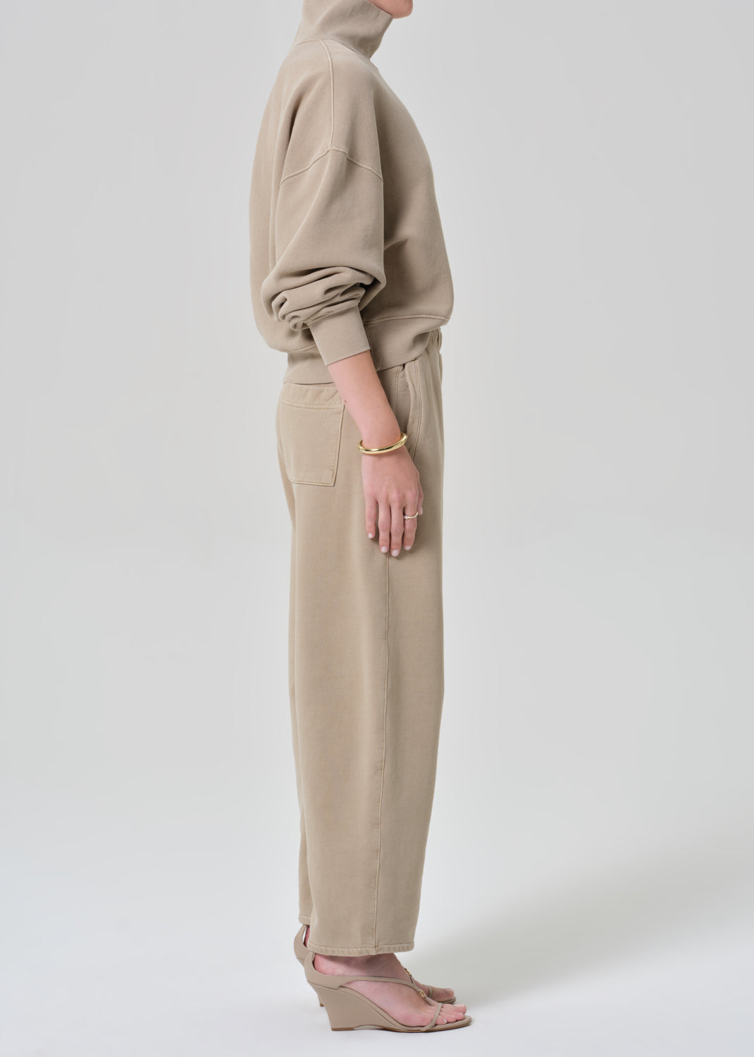 Person wearing a beige turtleneck sweater and pants on a grey background