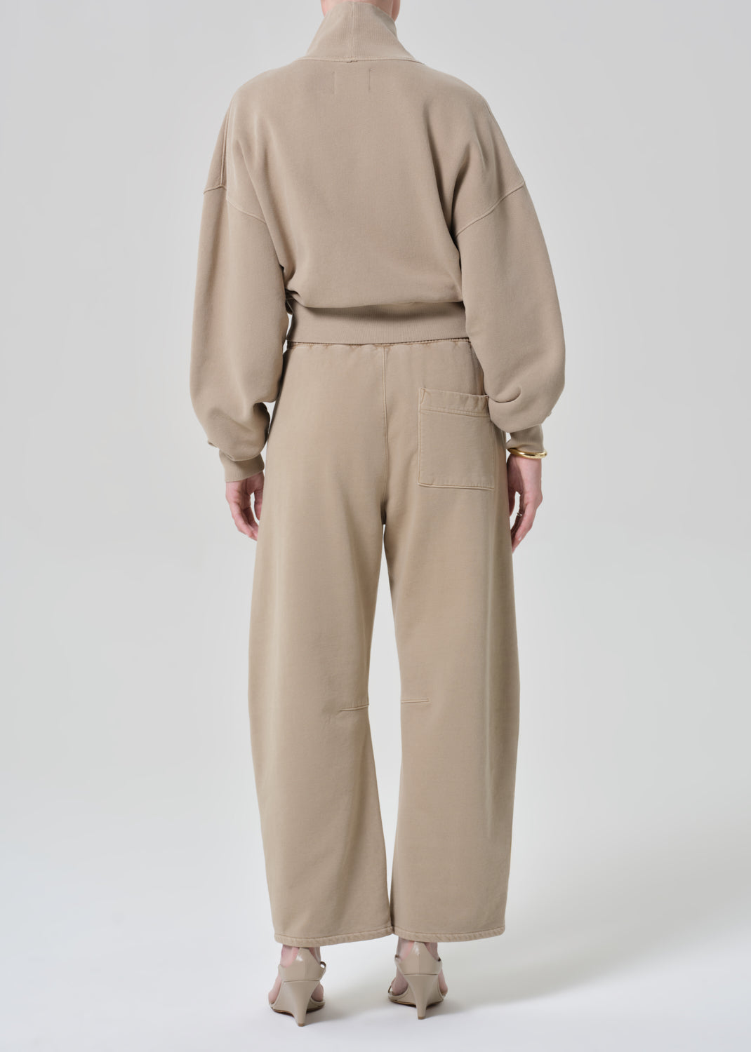 Person wearing a beige turtleneck sweater and pants on a grey background