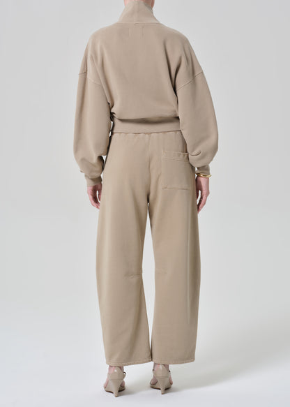 Person wearing a beige turtleneck sweater and pants on a grey background